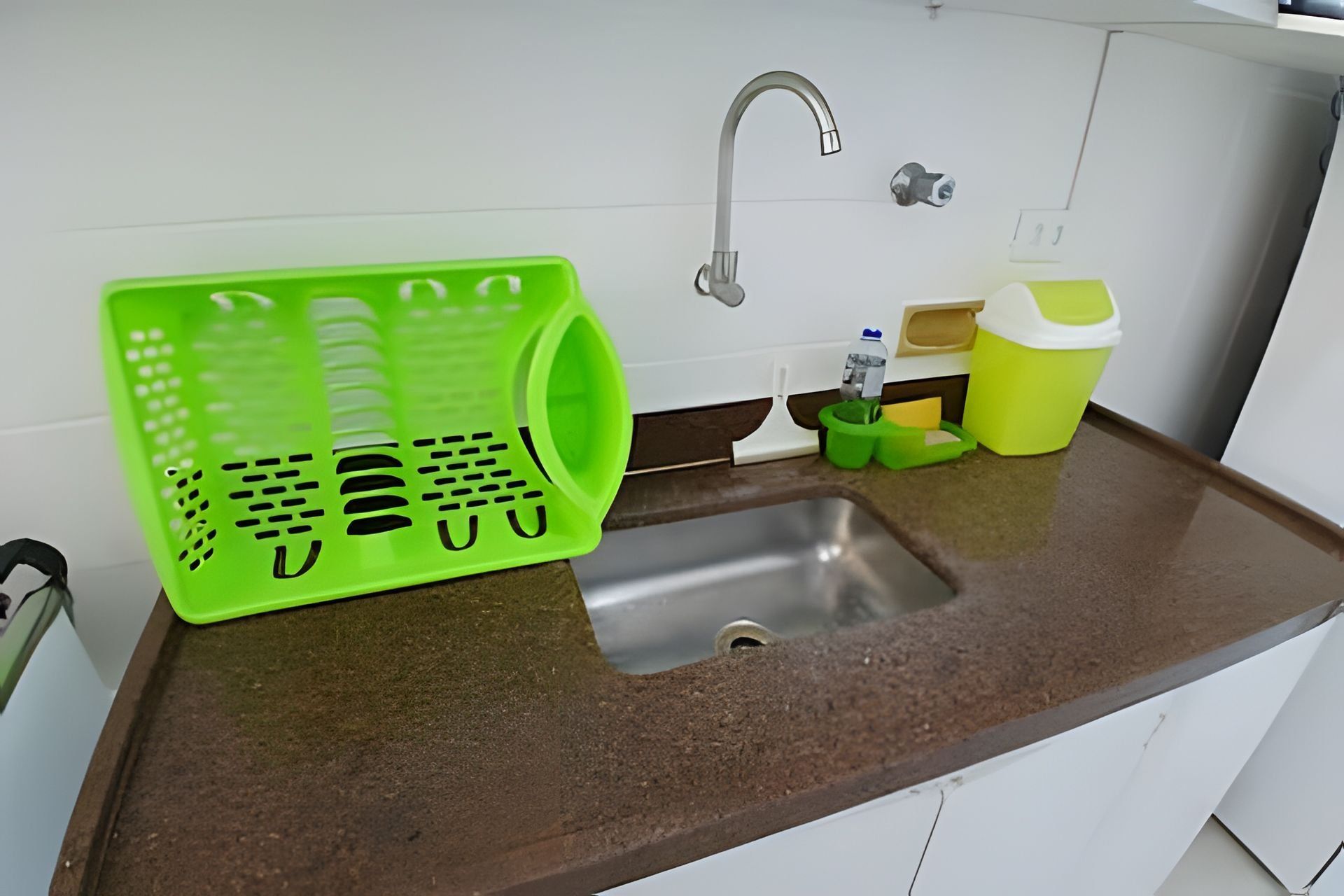 Uma cozinha com uma pia de aço inoxidável, uma cesta de plástico verde e um recipiente amarelo.