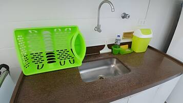 Uma cozinha com uma pia de aço inoxidável, uma cesta de plástico verde e um recipiente amarelo.