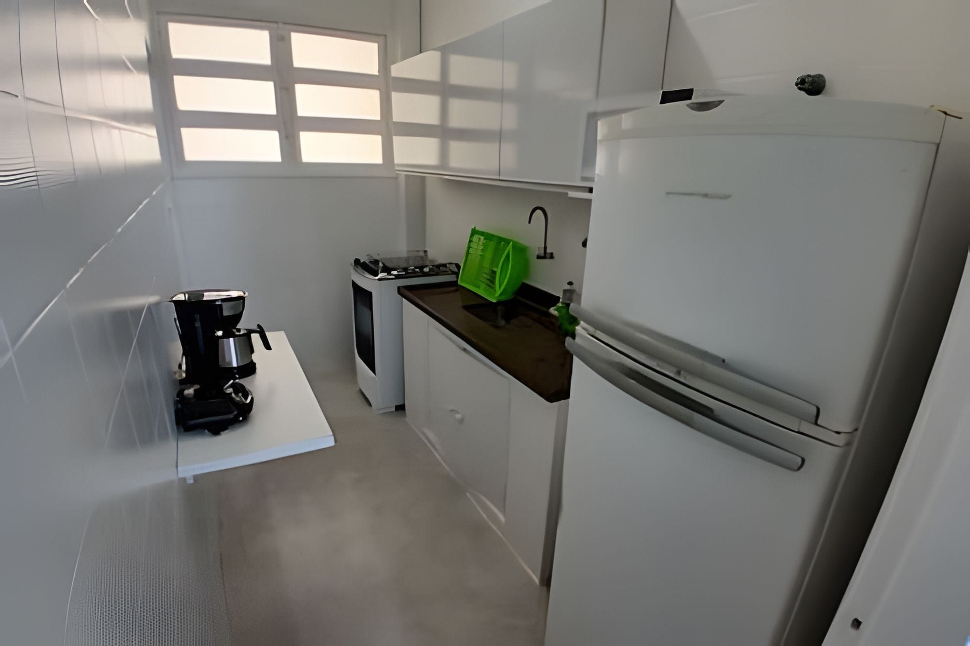 Una cocina compacta con armarios blancos, cafetera, estufa y refrigerador.