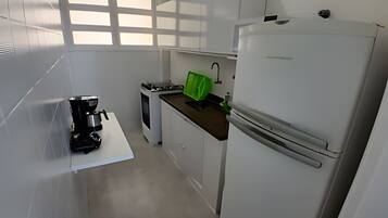 Una cocina compacta con armarios blancos, cafetera, estufa y refrigerador.