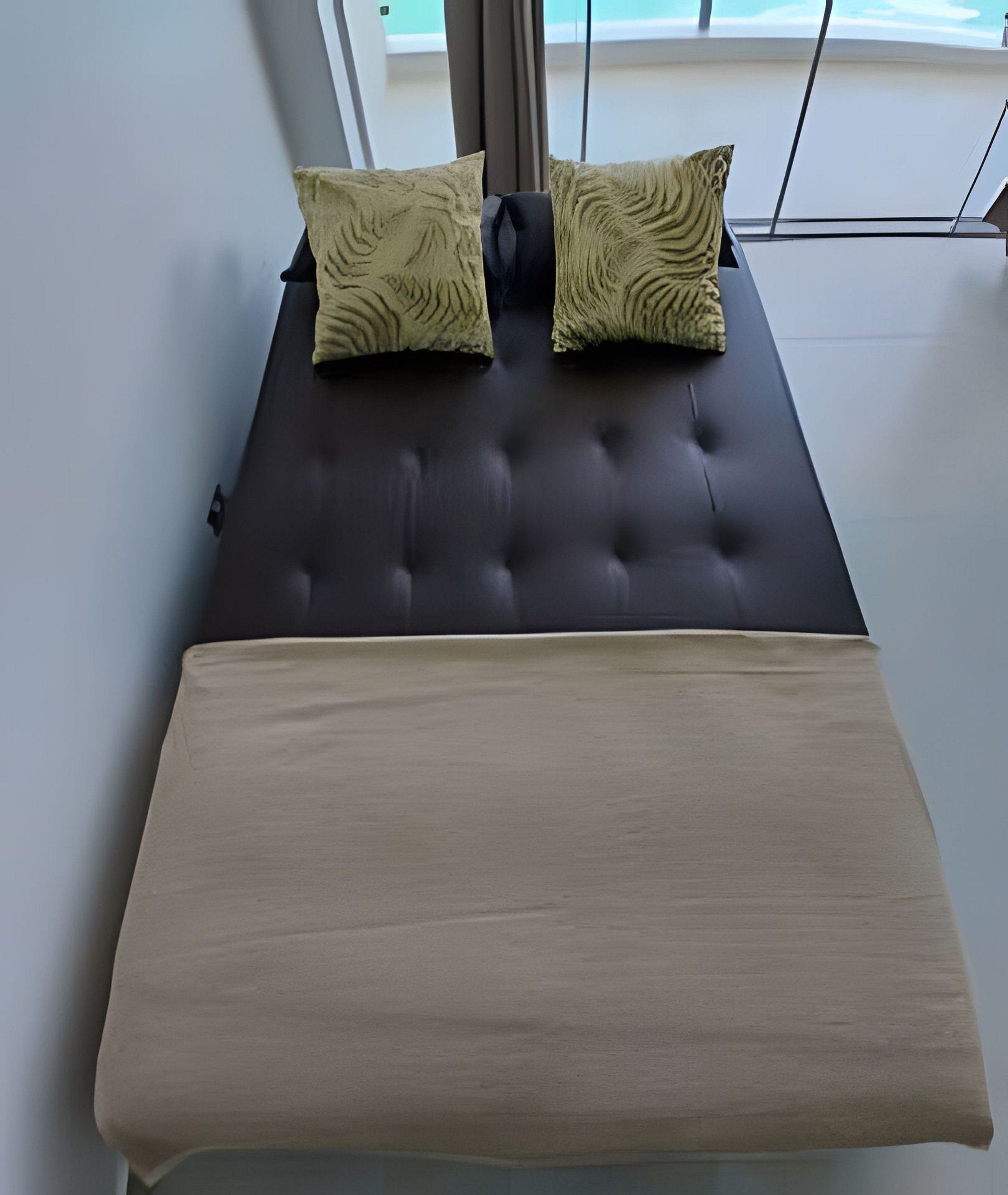 A modern bed with a dark headboard and two patterned pillows, a wooden headboard, and a view of the sky through a window.
