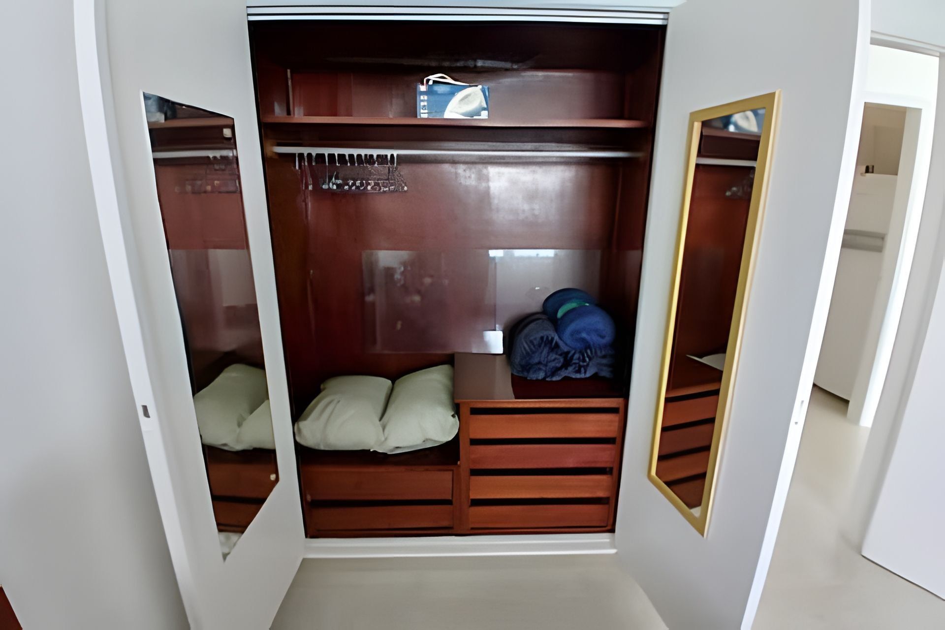 Un vestidor con puerta espejada, estantes de madera y un banco acolchado.