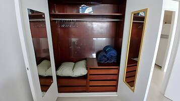 Un vestidor con puerta espejada, estantes de madera y un banco acolchado.
