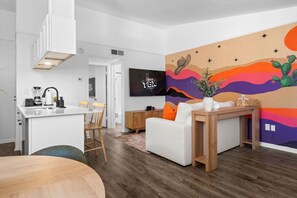 Ein modernes Wohnzimmer mit einem weißen Sofa, einem Holztisch und einem farbenfrohen Wandgemälde.