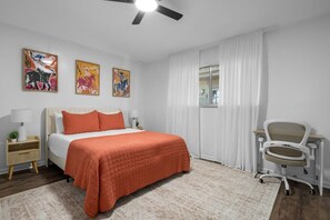 Ein Schlafzimmer mit einem Bett, einem Schreibtisch mit Stuhl, einem Deckenventilator und drei an der Wand hängenden Bildern.