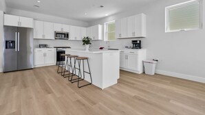 Eine moderne Küche mit weißen Schränken, einem Edelstahl-Kühlschrank, einer Mikrowelle und einer Kaffeemaschine.