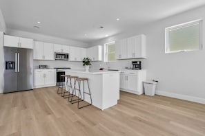 Eine moderne Küche mit weißen Schränken, einem Edelstahl-Kühlschrank, einer Mikrowelle und einer Kaffeemaschine.
