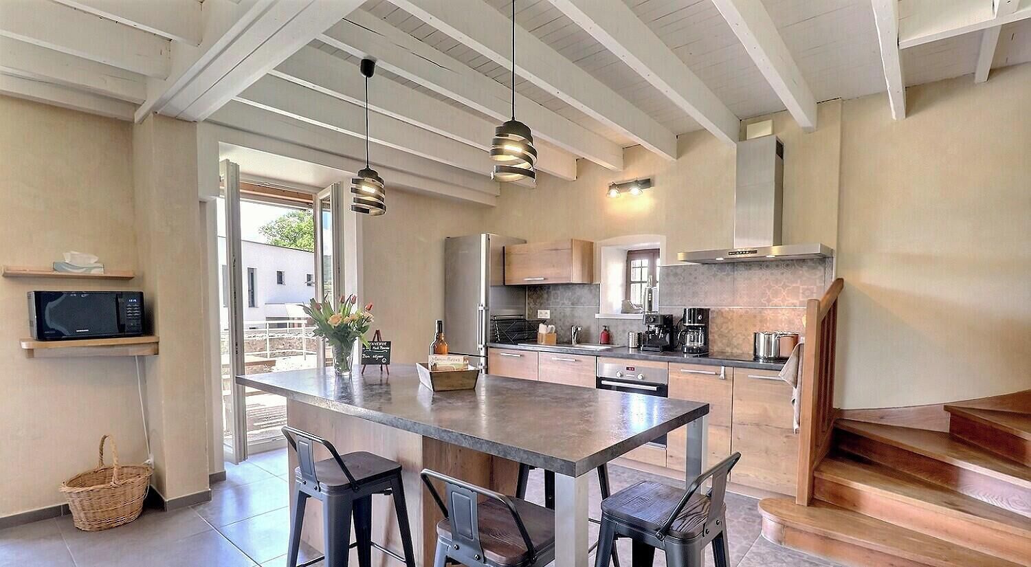 A modern kitchen with a central island, bar stools, hanging pendant lights, and a view of the outdoors.