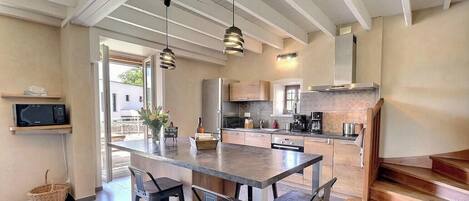 A modern kitchen with a central island, bar stools, hanging pendant lights, and a view of the outdoors.