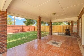 Ein überdachter Patio-Bereich mit Fliesenboden in Sternenmuster, Ziegelstützsäulen und einem Holzzaun im Hintergrund.