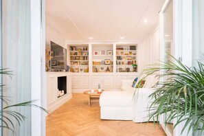 Ein Wohnzimmer mit einem weißen Sofa, einem Couchtisch und einem Bücherregal voller Bücher und Dekoration.