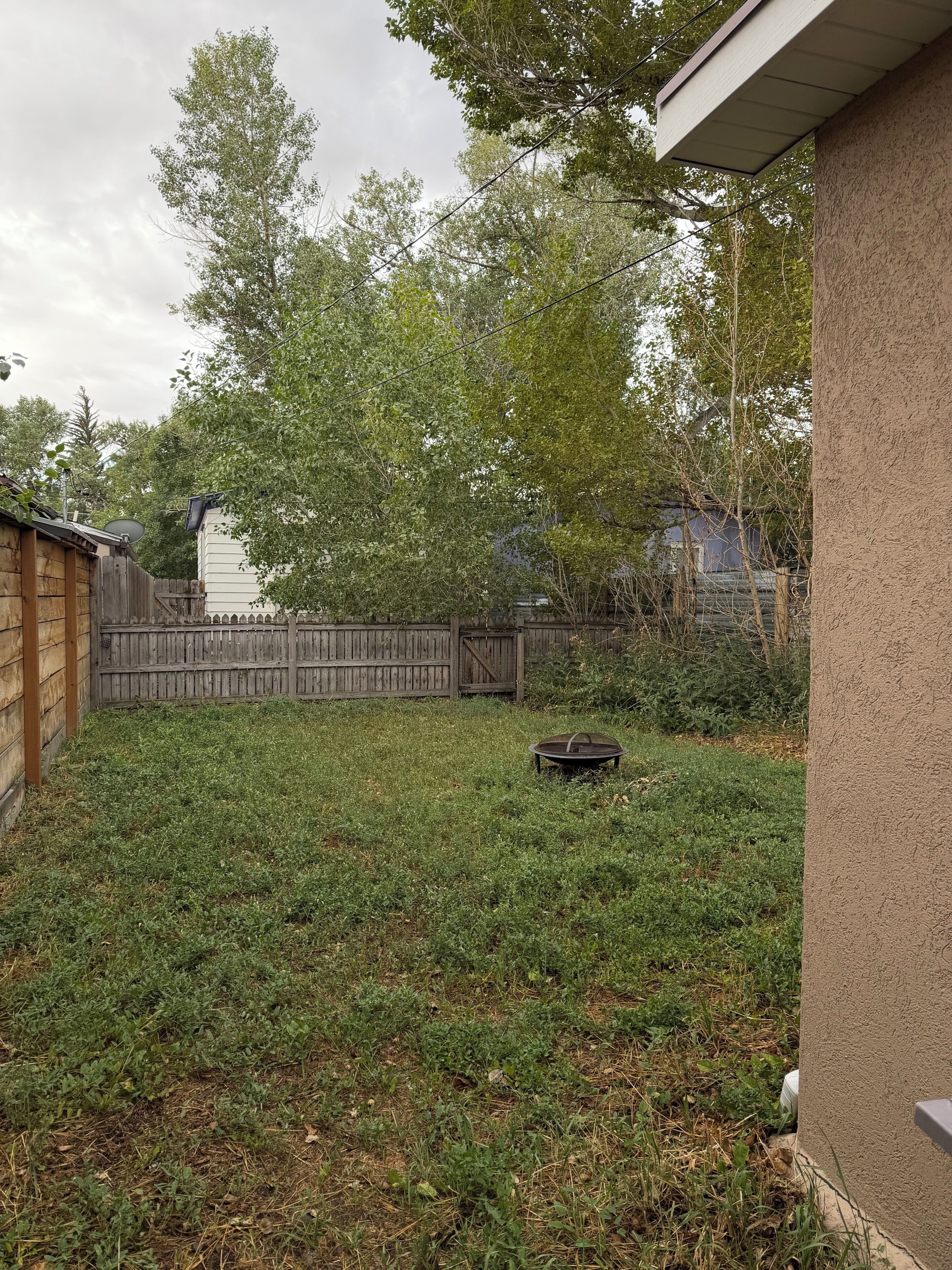 A backyard with a wooden fence, a metal grill, and a grassy lawn.