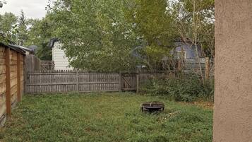 A backyard with a wooden fence, a metal grill, and a grassy lawn.