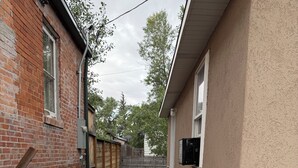 Un sendero de concreto estrecho bordeado por un edificio de ladrillo y uno de estuco con una cerca de alambre.