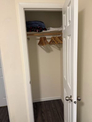 A closet with hanging clothes and a wooden shelf.