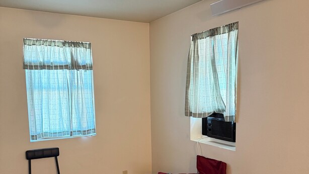 Una habitación con dos ventanas, una silla, un escritorio y una silla plegable roja.