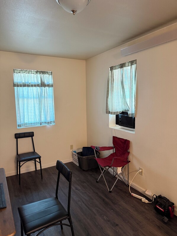 A room with two windows, a chair, a desk, and a red folding chair.