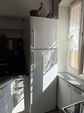 A kitchen with a white refrigerator, a window with sheer curtains, and a granite countertop. - Spacious Apartment with Mountain Views - Free Parking - Near ÎLE ROUSSE (Belgodère)