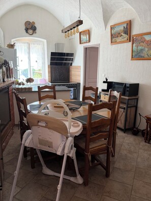 A dining area with a round table, chairs, a high chair, a kitchen with a stove, and a microwave. - Spacious Apartment with Mountain Views - Free Parking - Near ÎLE ROUSSE (Belgodère)