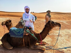 A person riding a camel in a desert with sand dunes in the background.