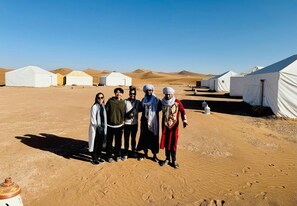 A group of people standing in a desert with white tents in the background.