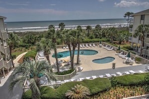 Een resort met een zwembad, palmbomen en uitzicht op het strand.