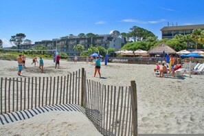 Een strandvolleybalveld met een houten hek op de voorgrond, strandparasols en ligbedden op de achtergrond.
