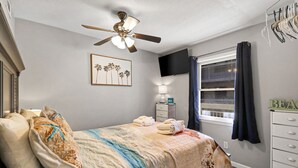 A bedroom with a bed, a ceiling fan, a TV, a window with curtains, and a dresser. - Breakers 220 Oceanfront Condo Direct Beach Access Elevator (Hilton Head Island)