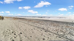 A beach with a wide sandy area, a few people walking, and a clear sky with clouds. - Breakers 220 Oceanfront Condo Direct Beach Access Elevator (Hilton Head Island)