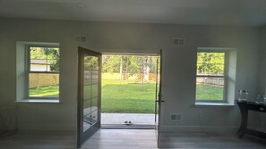 Ein Zimmer mit einer Tür, die in einen Garten führt, einem Fenster links und einem Fenster rechts.