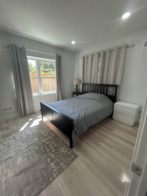 A bedroom with a bed, a nightstand, a lamp, a window with curtains, and a small white cabinet. - Private 2BR/1.5BA Guest Suite w Elevator Nr Metro, Tysons Corner, Falls Church (Dunn Loring)