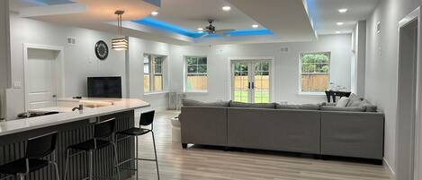 Eine moderne Küche mit Barbereich, einem grauen Sofa und einem Deckenventilator.