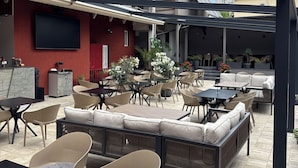 An outdoor patio area with multiple seating arrangements, including tables and sofas, and a flat-screen TV mounted on the wall.