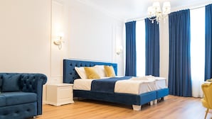 A hotel room with a bed, bedside tables, a sofa, and a chandelier.