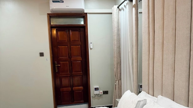 A bedroom with a bed, a wooden door, an air conditioning unit, and a light fixture.