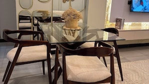 A modern dining area with a glass table surrounded by wooden chairs, a decorative vase, and wall-mounted mirrors.