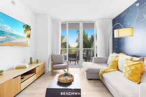 A modern living room with a beach view, a sofa, a coffee table, and a dining area. - Intracoastal 2BR - Pool, Resort & Private Balcony (Hallandale Beach)
