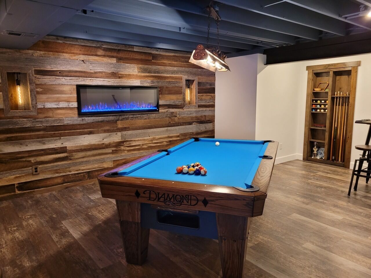 Ein Billardtisch mit der Aufschrift 'DIAMOND', ein blau beleuchteter Kamin und eine Holzwand mit eingebauten Regalen.
