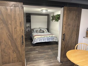 Ein Zimmer mit einem Bett, einer Holztür, einem kleinen Tisch und einer hängenden Pflanze.