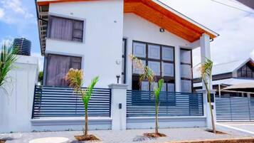 Une maison moderne à deux étages, dotée d’un toit plat, de grandes fenêtres et d’un balcon.