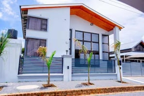 A modern two-story house with a flat roof, large windows, and a balcony.