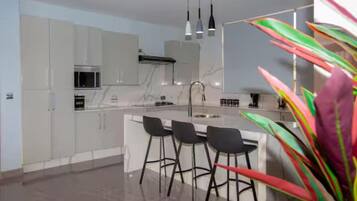 A modern kitchen with white cabinets, a central island with bar stools, and pendant lighting.