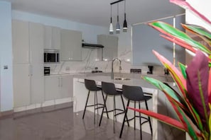 A modern kitchen with white cabinets, a central island with bar stools, and pendant lighting.