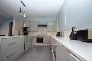 Una cocina moderna con armarios blancos, horno integrado y cafetera.