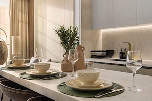 A modern kitchen with a long countertop, a potted plant, and a wine glass. - Stylish 1BR Dubai with Pool, Gym, Padel & Balcony (Jumeirah Village Circle)
