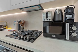 A modern kitchen with a gas stove, a microwave, a toaster, and a kettle. - Stylish 1BR Dubai with Pool, Gym, Padel & Balcony (Jumeirah Village Circle)