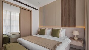 Hotellihuone, jossa on suuri sänky, yöpöytä lampun kanssa, peili ja näkymä ulos.