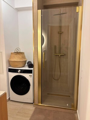 Ein modernes Badezimmer mit einer Glaskabine zur Dusche, einer Waschmaschine und einem Korb am Boden.
