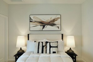 A bedroom with a bed, two bedside lamps, a headboard, and a framed abstract painting above the bed. - Downtown Skyline Views | Rooftop Patio | Sleeps 7+ (Des Moines)