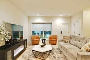 A living room with a flat-screen TV, two armchairs, a sofa, a coffee table, and a large window with blinds. - Downtown Skyline Views | Rooftop Patio | Sleeps 7+ (Des Moines)